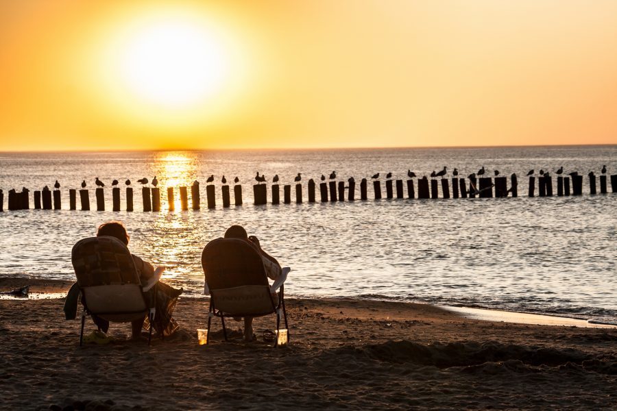 dwoje ludzi na leżakach na plaży w mielnie o zachodzie słońca